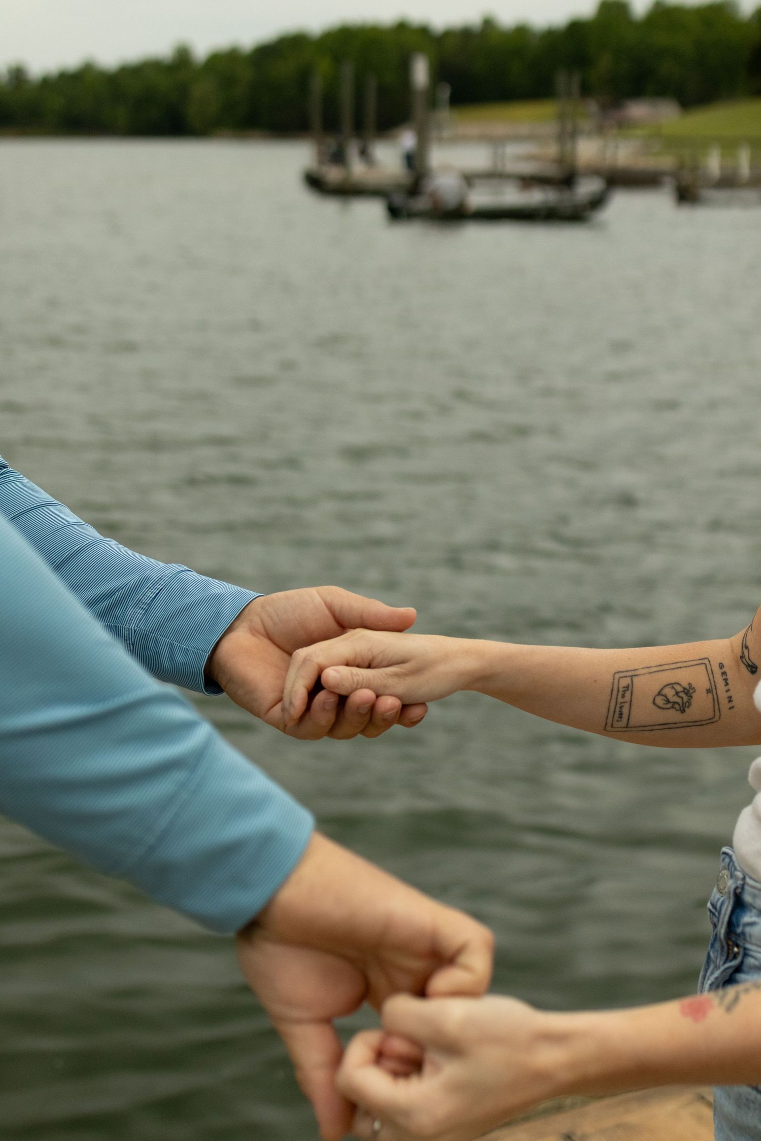 Two people reach out to hold hands with lake and dock in background.