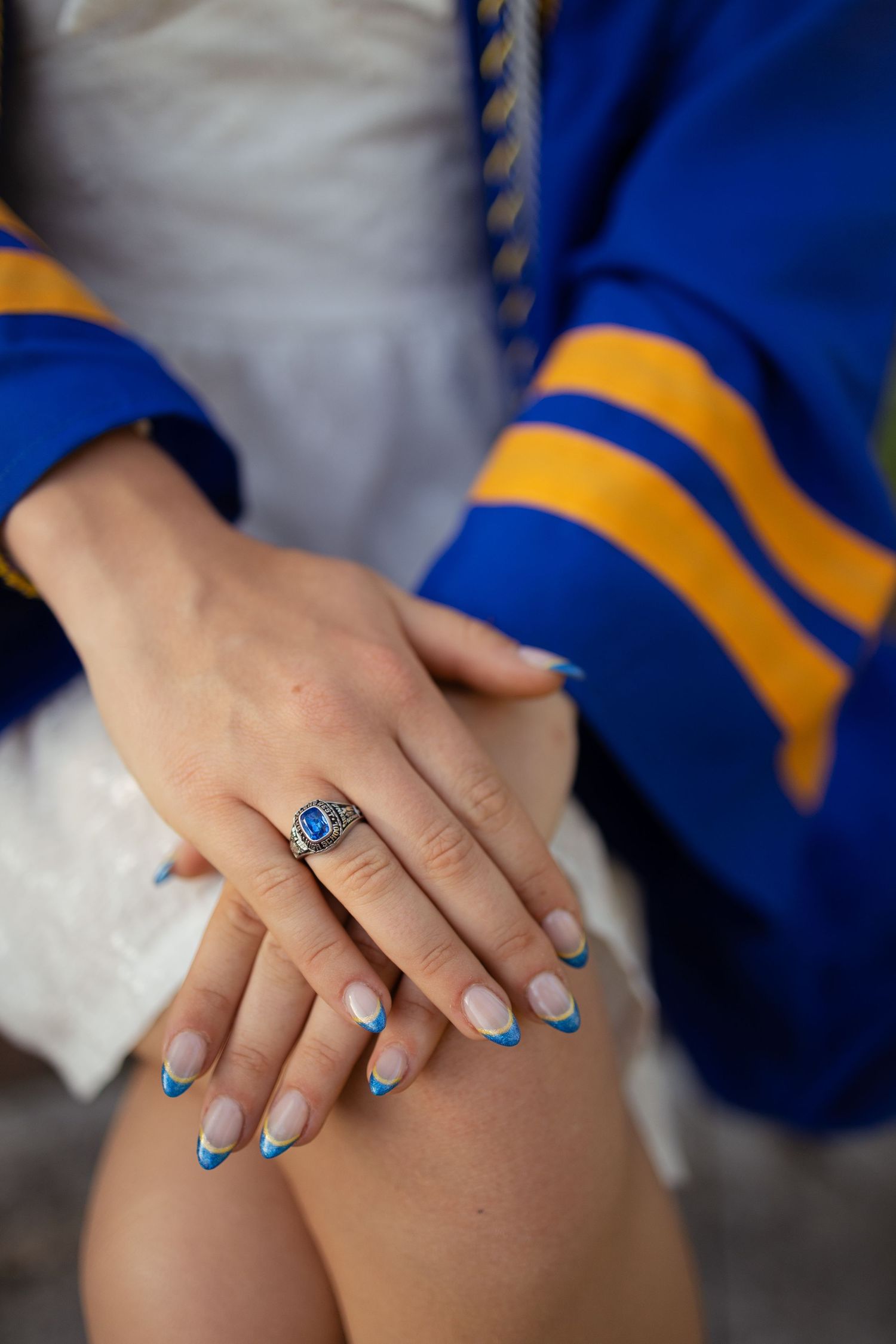 Close-up of hands with blue nail polish and ring wearing graduation honors cords.