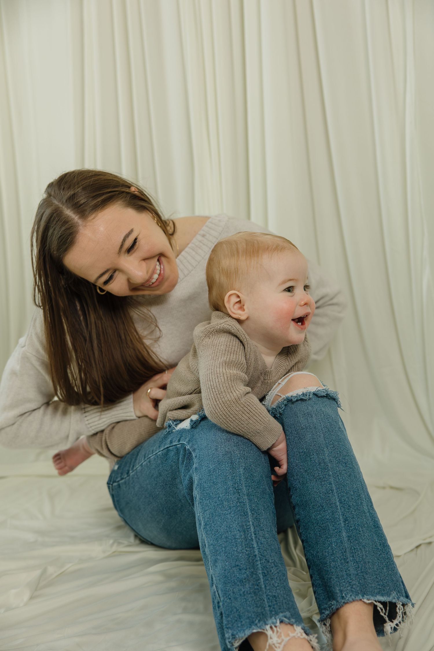 Joyful playtime on white sheets with matching beige sweaters and casual denim.