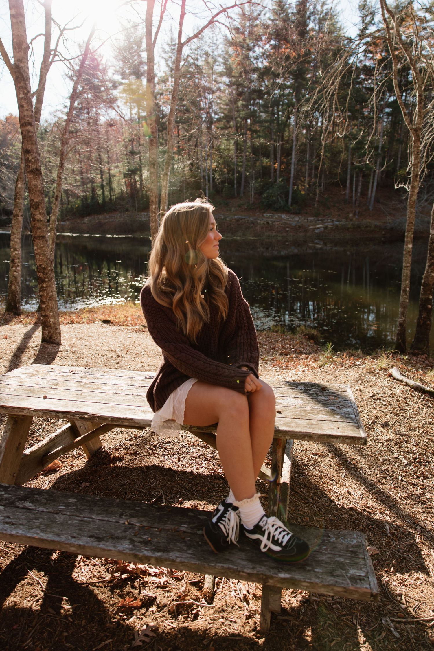 Rustic wooden bench surrounded by fallen autumn leaves beside a tranquil lake.