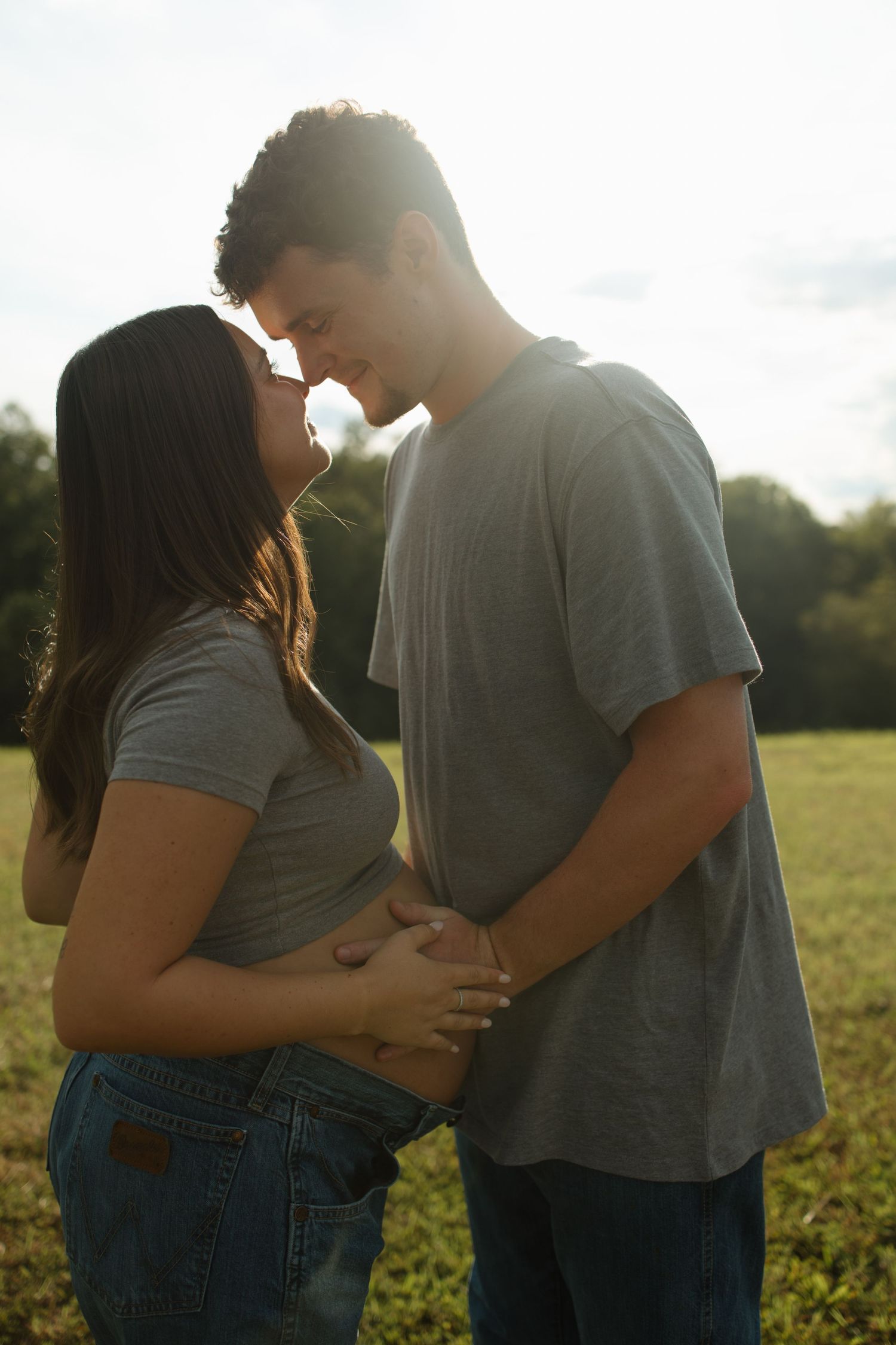 Expectant couple sharing intimate moment in sunlit field.