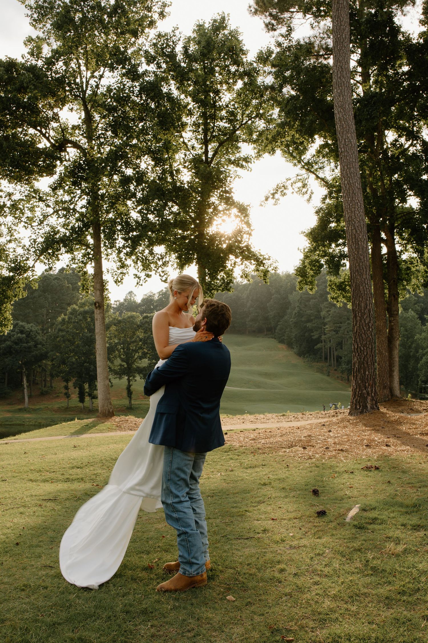 A romantic sunset moment captured between newlyweds on a grassy hillside.