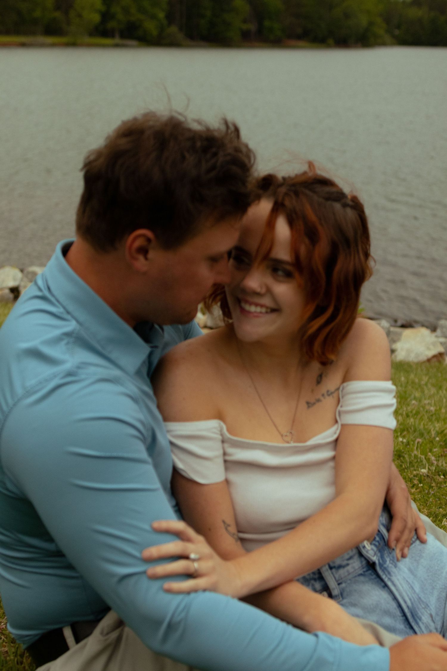 A tender moment shared between two people sitting on grass by the water.