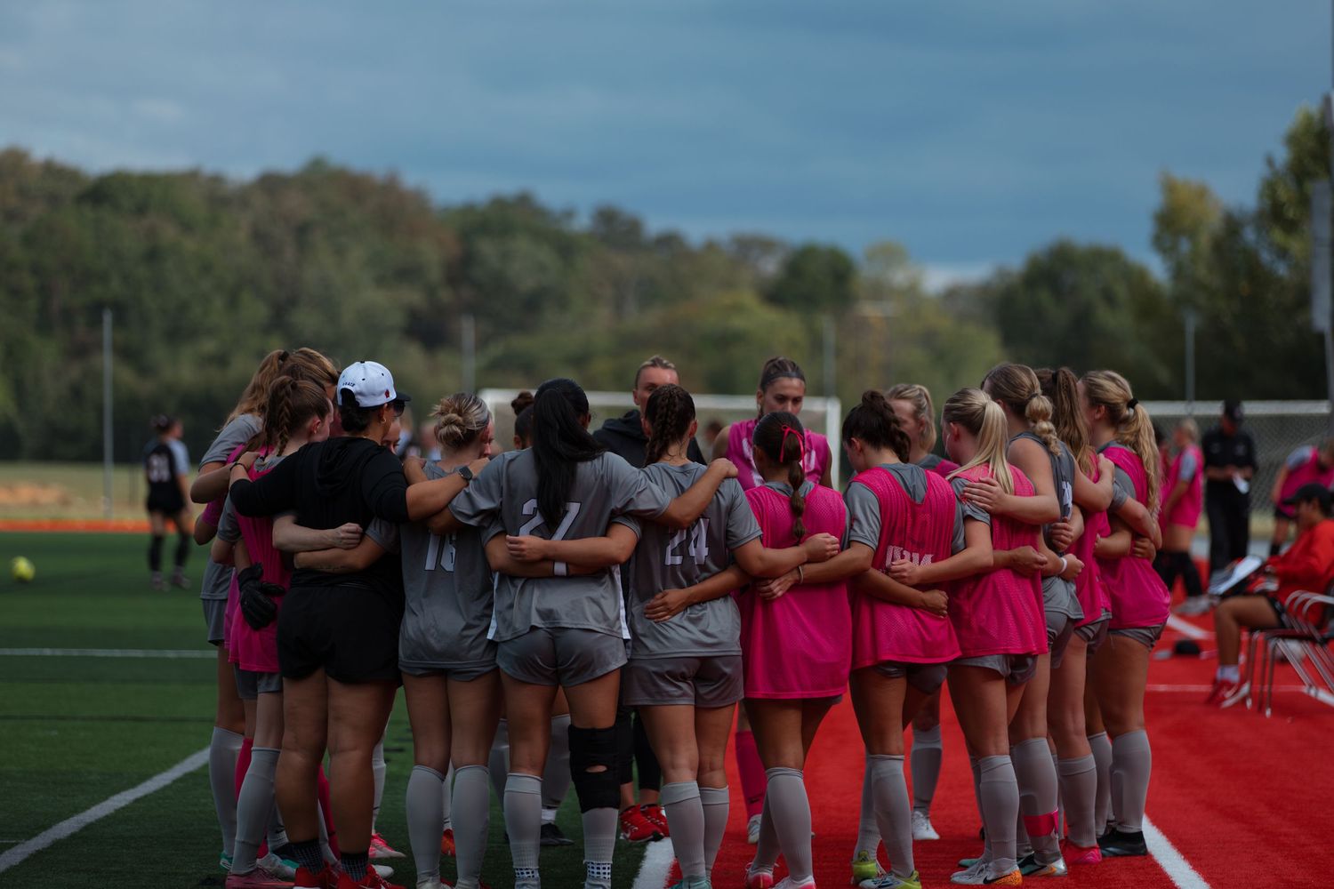 Soccer team huddled together in unity wearing pink and gray uniforms.