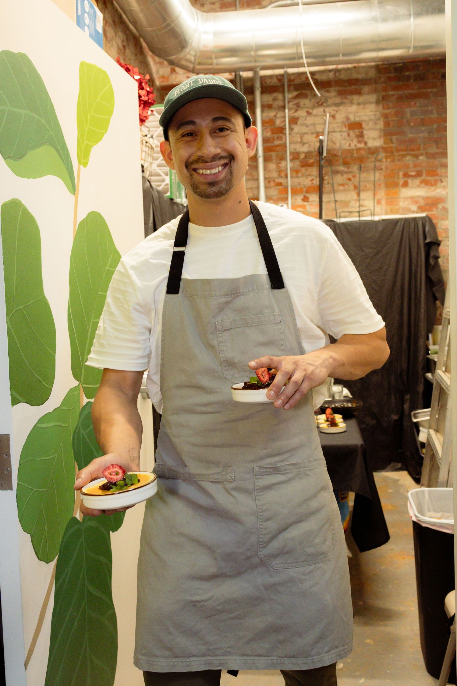 Chef in grey apron serving plated dishes in restaurant setting.