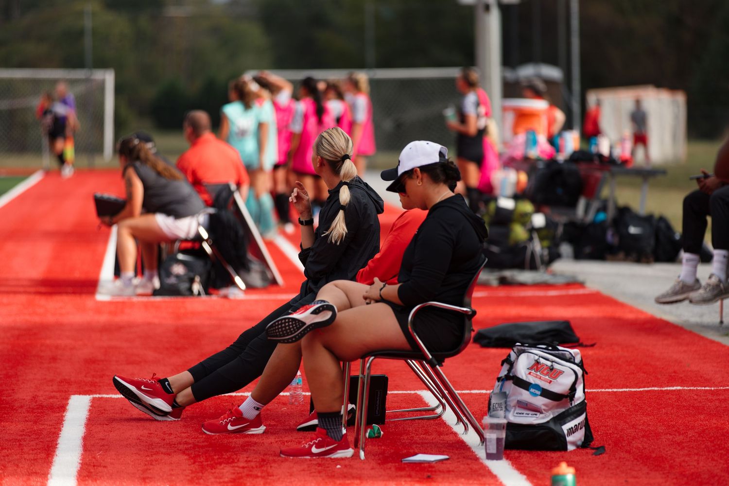 Athletes performing stretching exercises on red turf field.