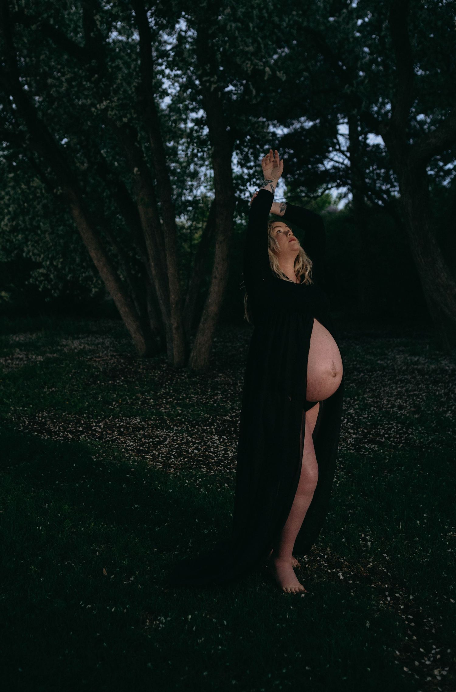 Figure in black dress moving through a dark wooded area at twilight.