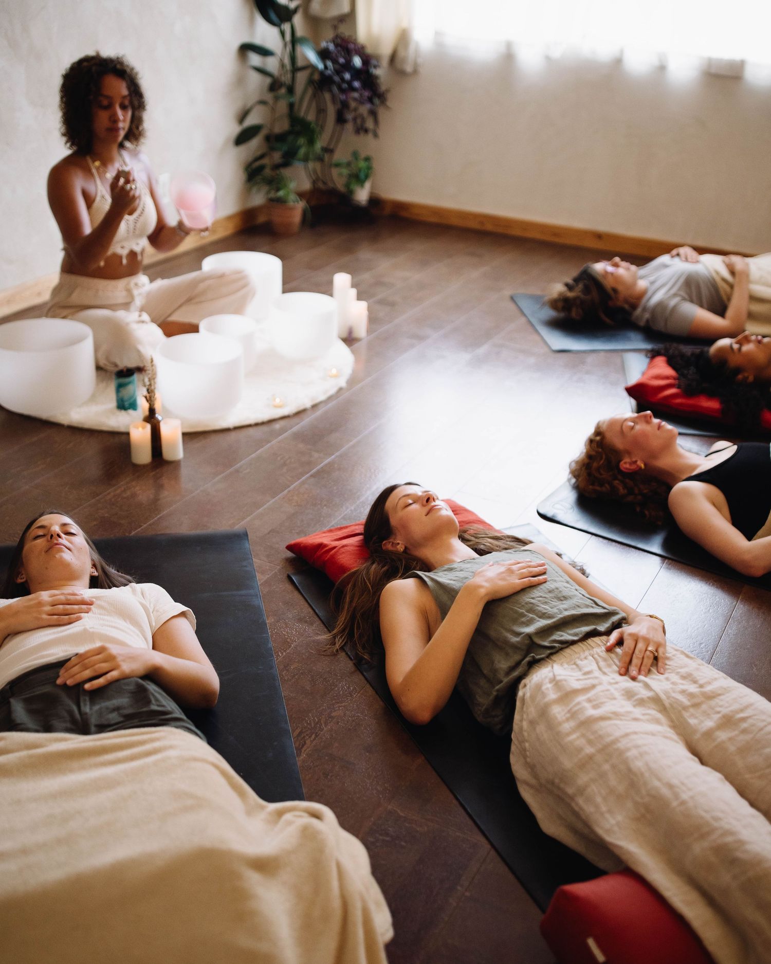 Group of women lying on yoga mats during a sound bath meditation session with singing bowls and candles.