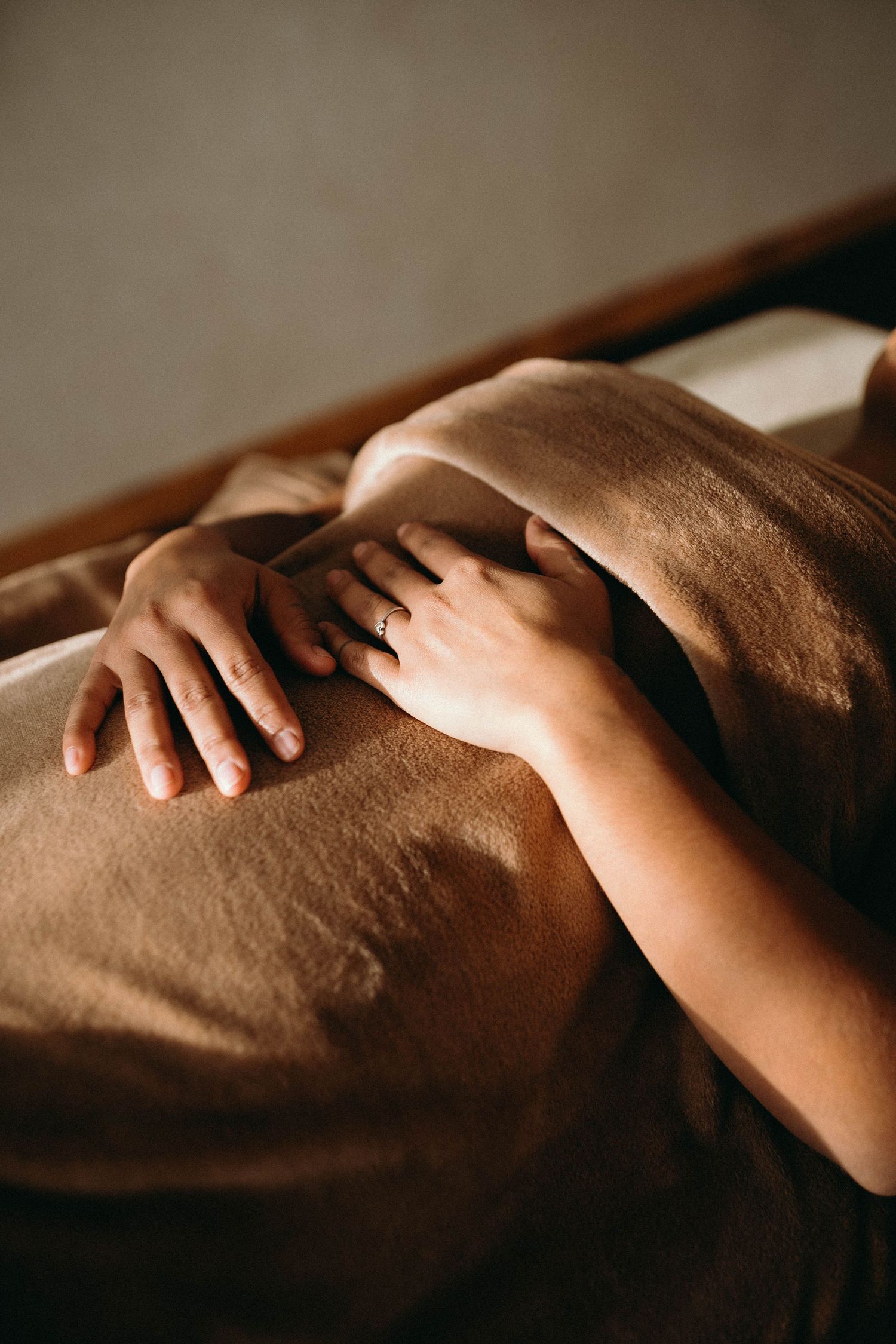 A massage therapist's hands gently working on a client's back draped in a soft brown towel on a spa table.
