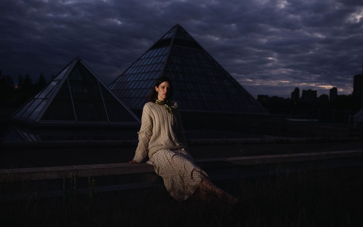 Modern glass pyramid structures stand against a moody twilight sky.