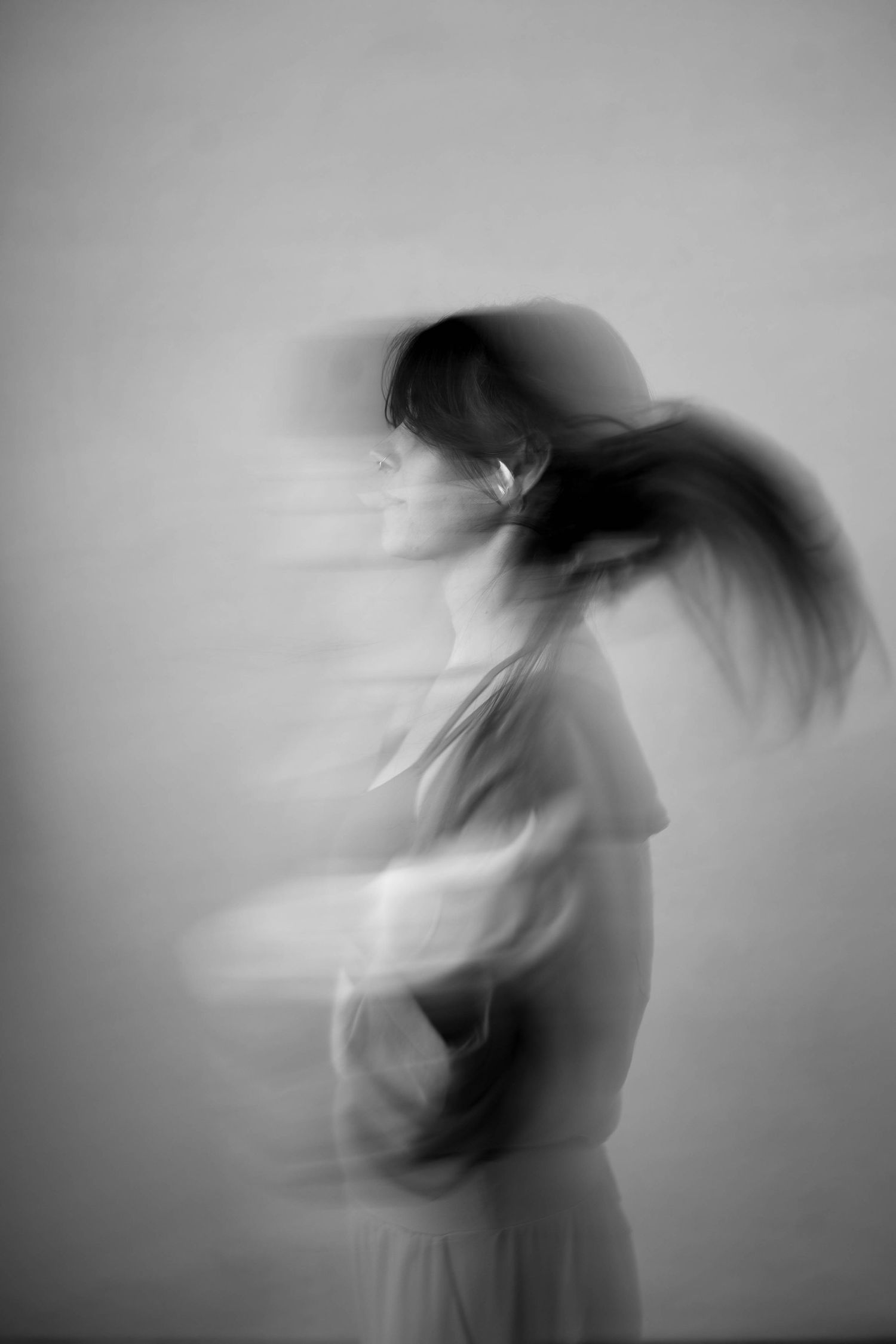 Black and white motion blur photo of a woman tossing her hair, creating a ghostly artistic effect.