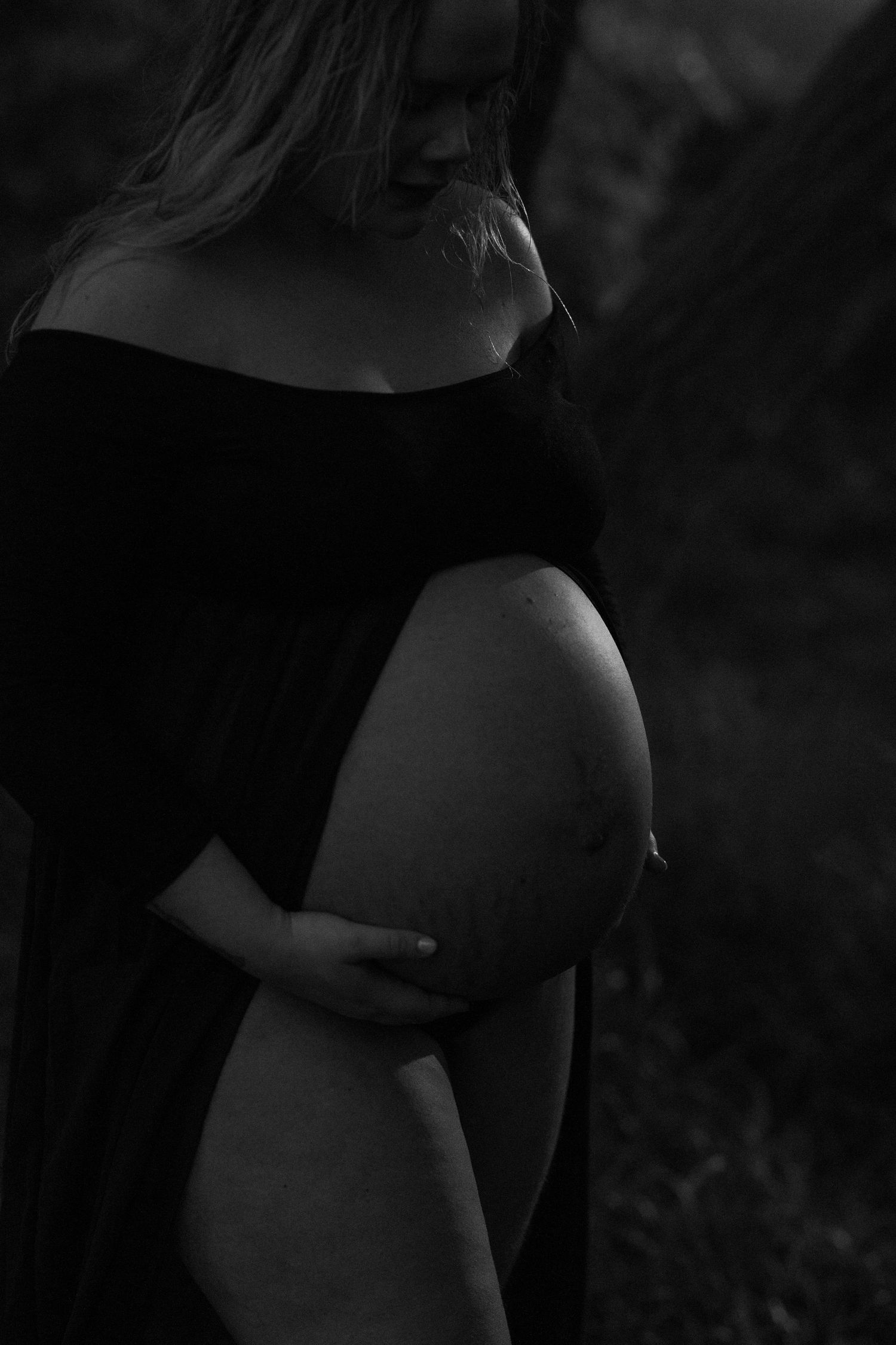Black and white maternity silhouette showcasing a pregnant belly in dramatic lighting.