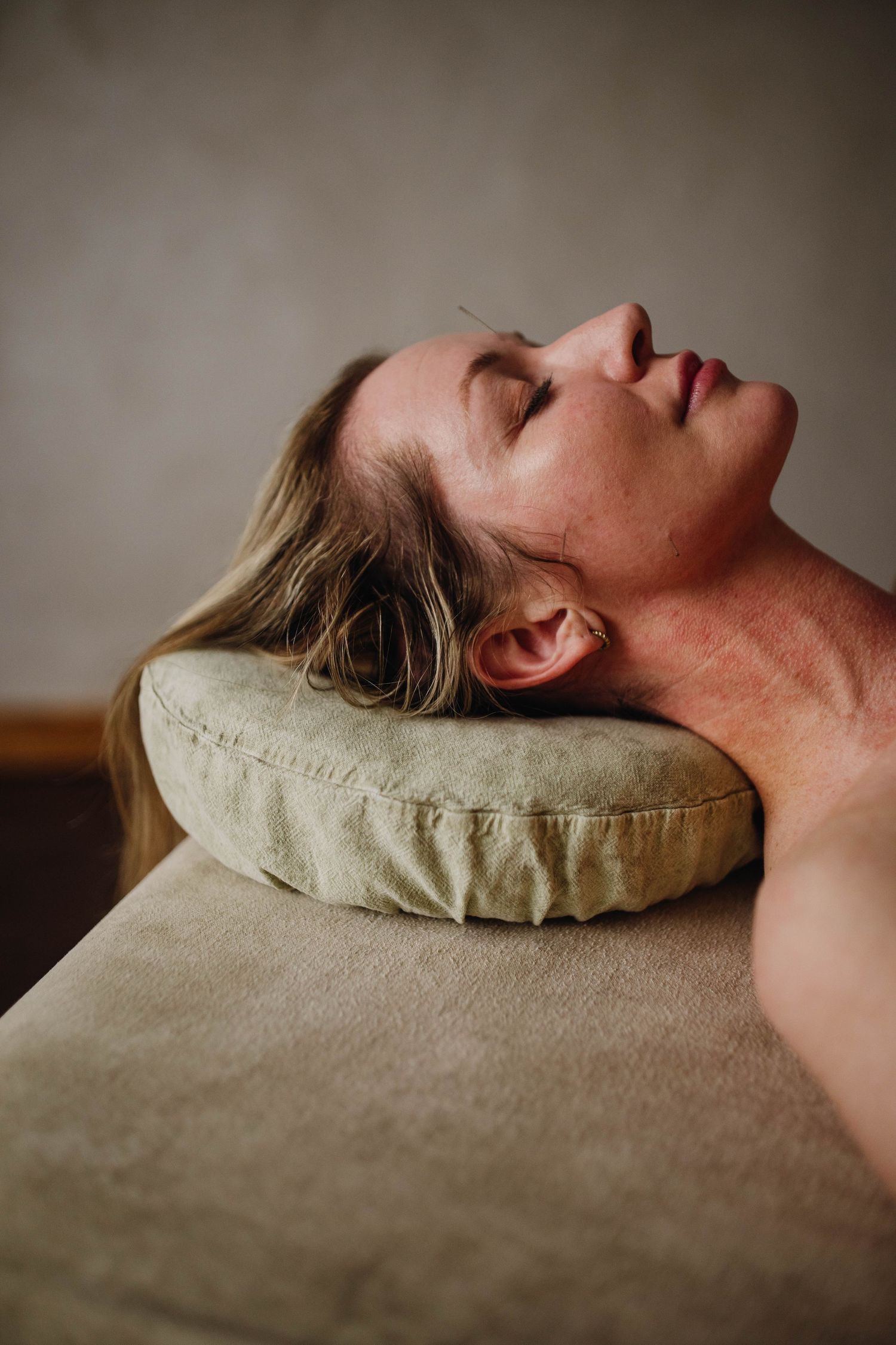 Woman lying on massage table with eyes closed, resting head on green pillow in a serene spa setting.