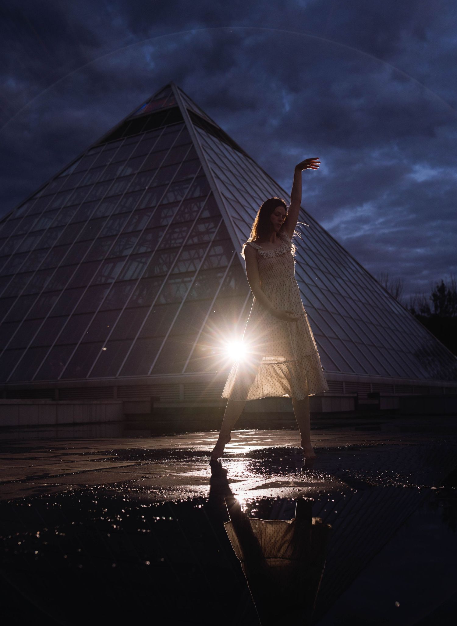 Artistic silhouette against a dramatic pyramid structure at dusk with light beams shining through.