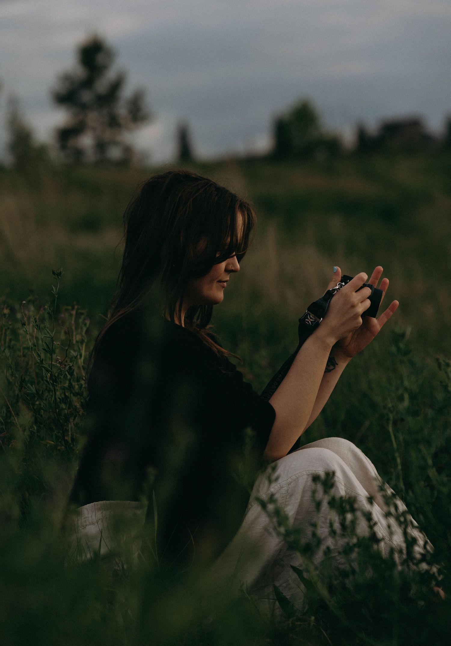 Person in dark clothing sitting in wild grass field at dusk.