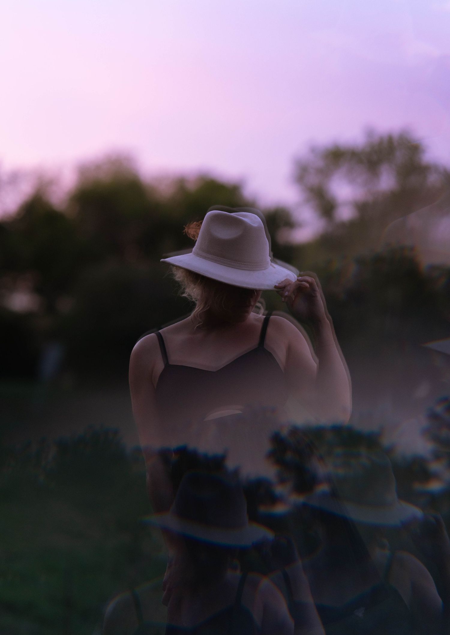 Silhouette in hat during purple sunset creates dramatic outdoor portrait.