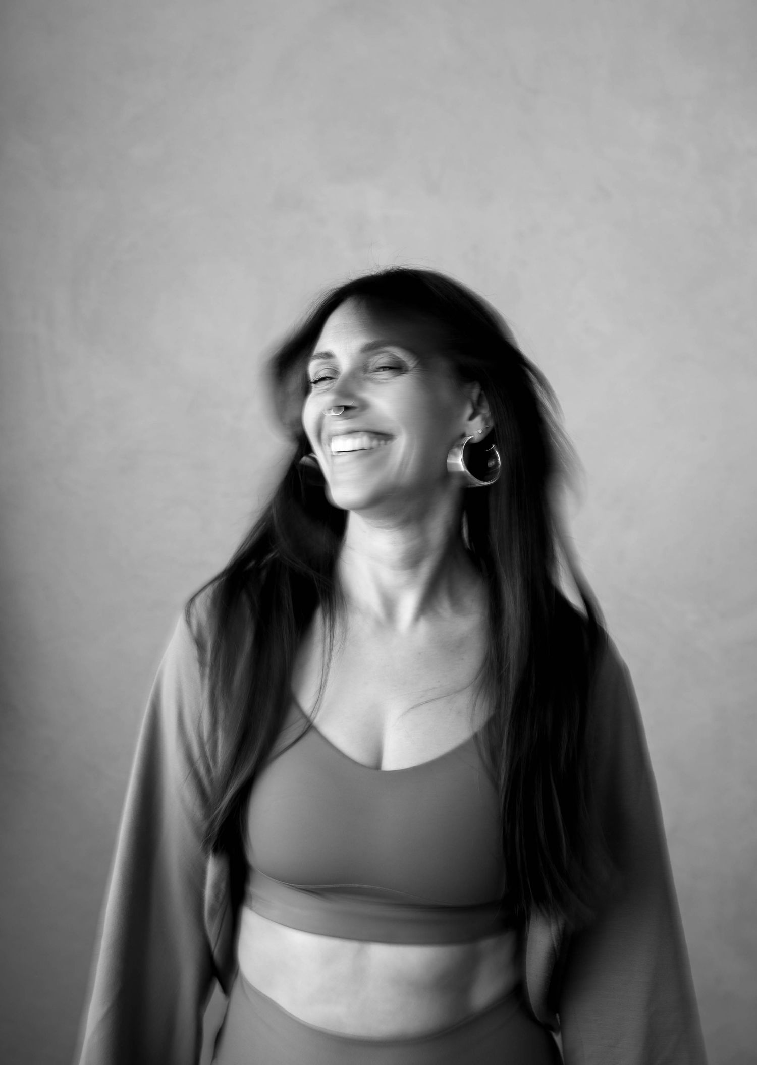 Black and white photo of a smiling woman with long dark hair wearing a crop top and hoop earrings.