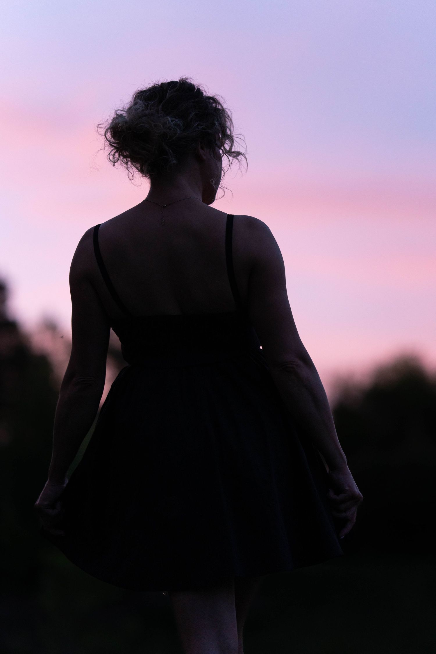 Silhouette of a person in a dress against a pink and purple sunset sky.
