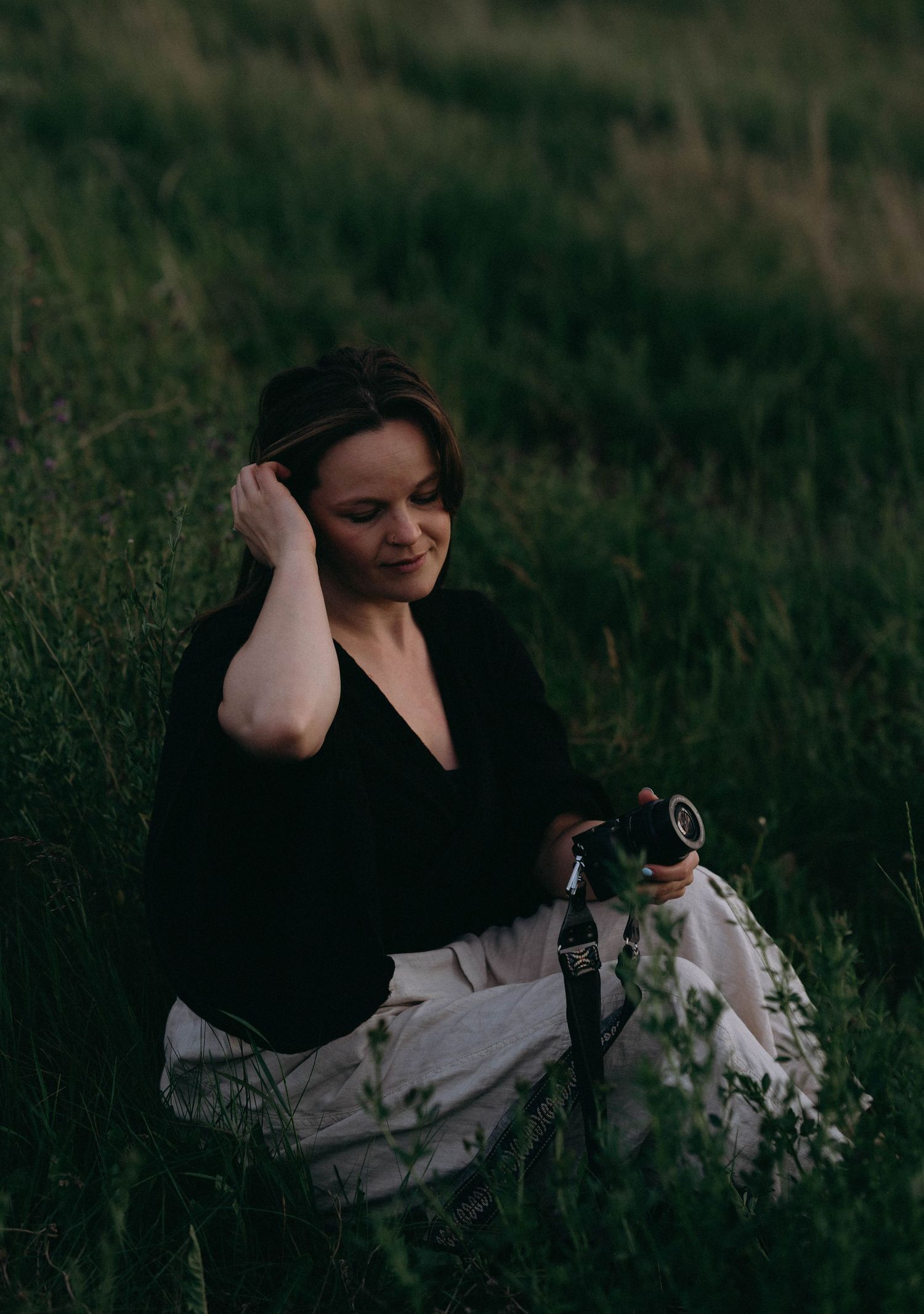 Woman in black flows attire reclines in a grassy meadow at dusk creating a dreamy outdoor portrait series.