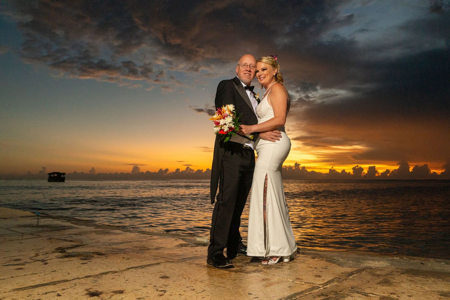 A wedding couple poses on a sandy beach during sunset with dramatic orange and purple skies in Negril.