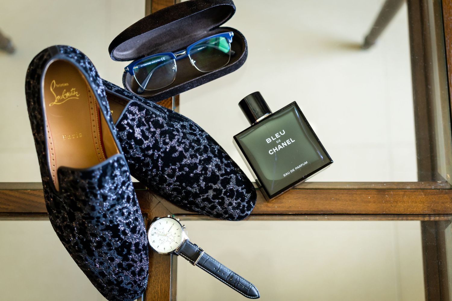 A pair of floral pattern blue loafer shoes with cologne bottle placed on a wooden surface.