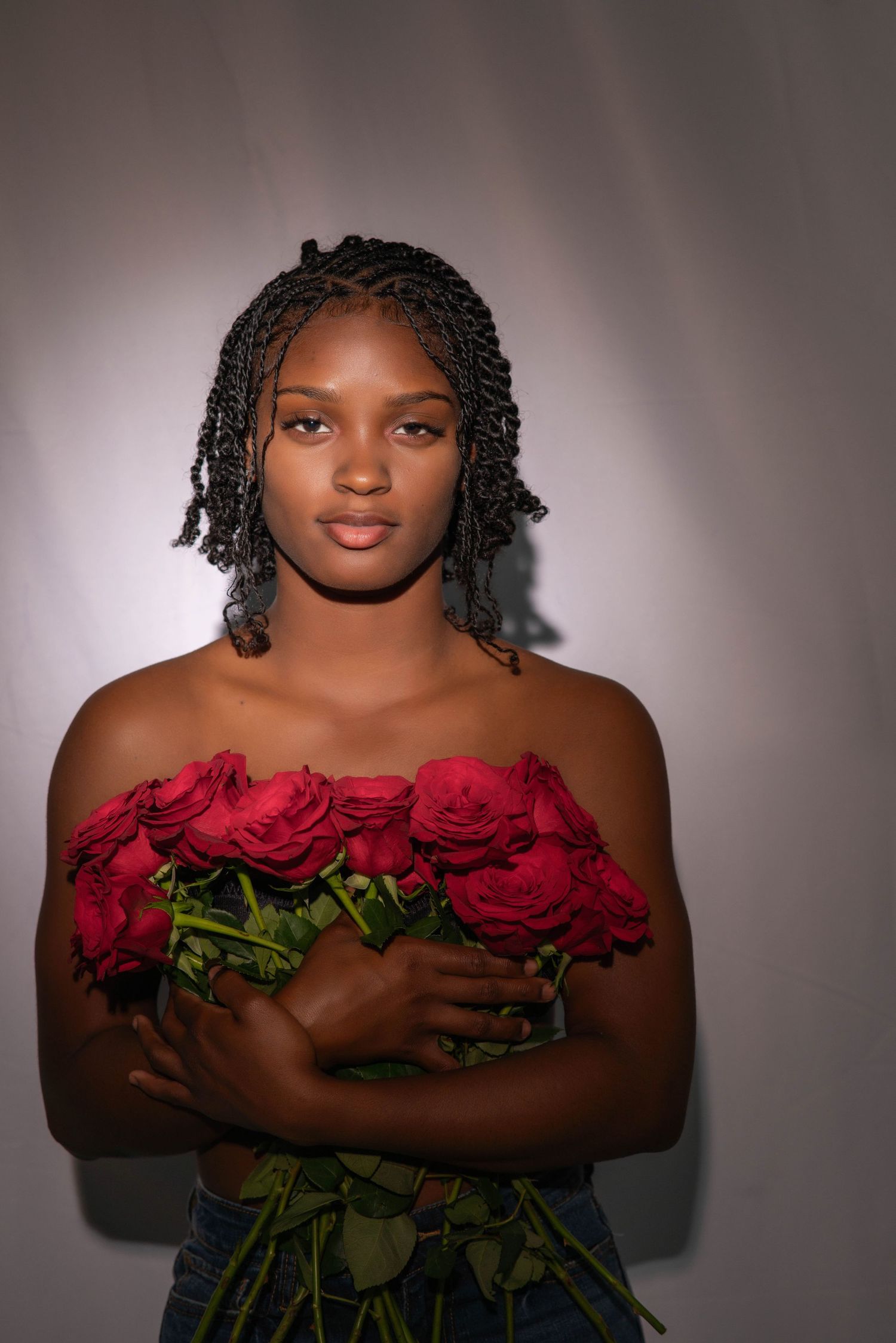 Young lady holding red roses against dark background in dramatic studio lighting during a Valentine's Day photo shoot.