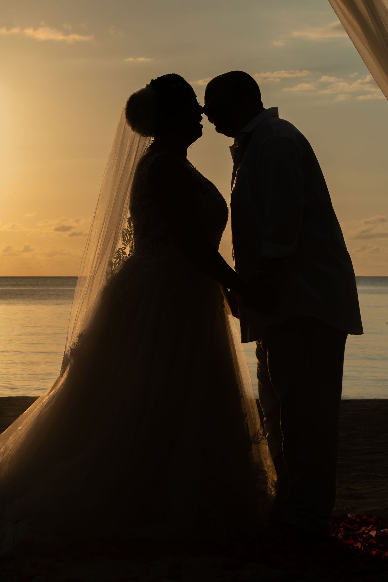 Silhouettes of a couple at sunset in wedding attire embracing against an ocean backdrop during golden hour.