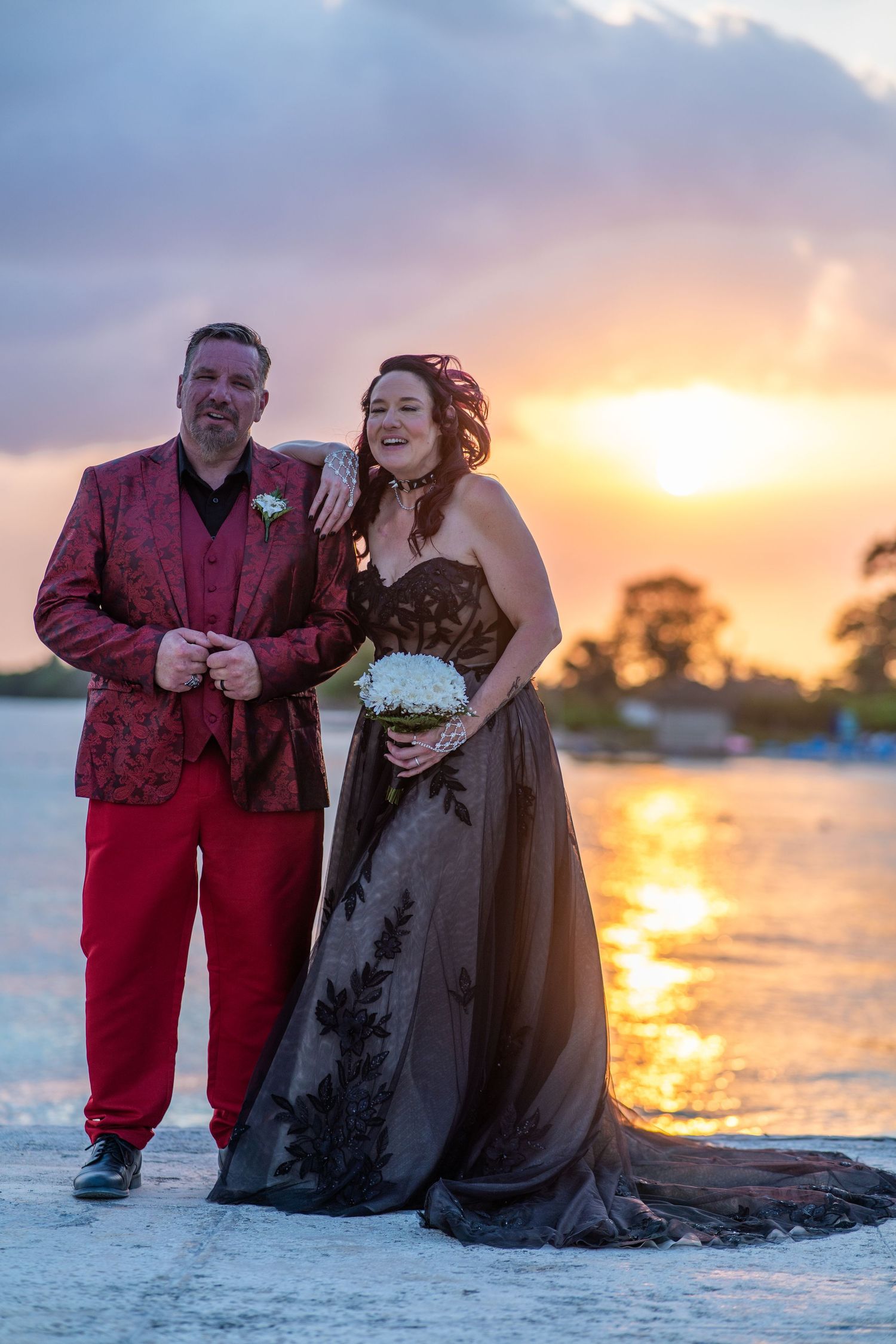 Couple posing on Negril beach at sunset wearing red and black formal attire while posing for romantic photos near ocean.