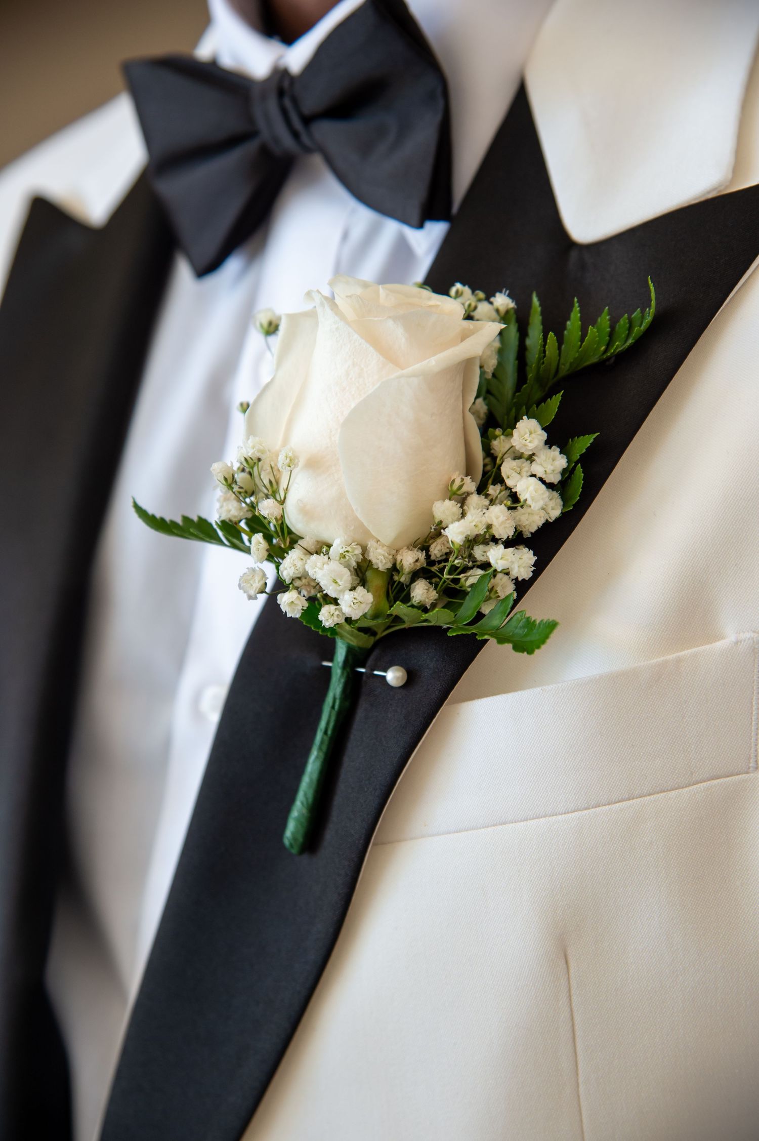 A row of groomsmen's boutonnieres with white roses and baby's breath against black tuxedo lapels.
