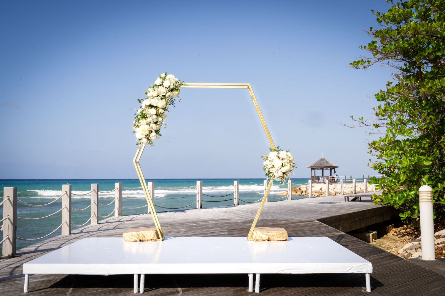 A collage of coastal wedding decorations with white floral arches and tropical beach views during a sunset ceremony.