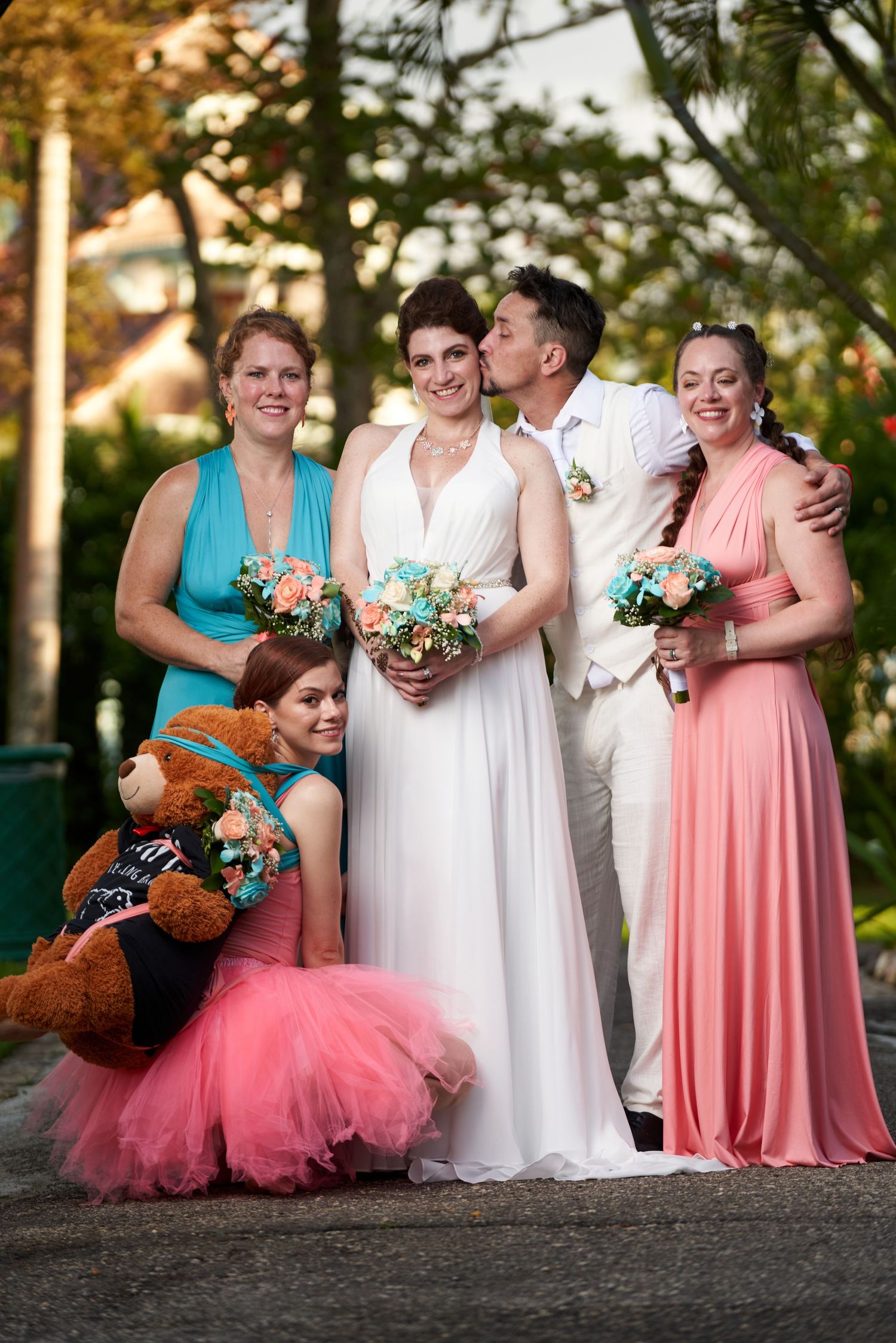 Wedding party poses together for casual candid photo series showing pink dresses and white gown during golden hour.