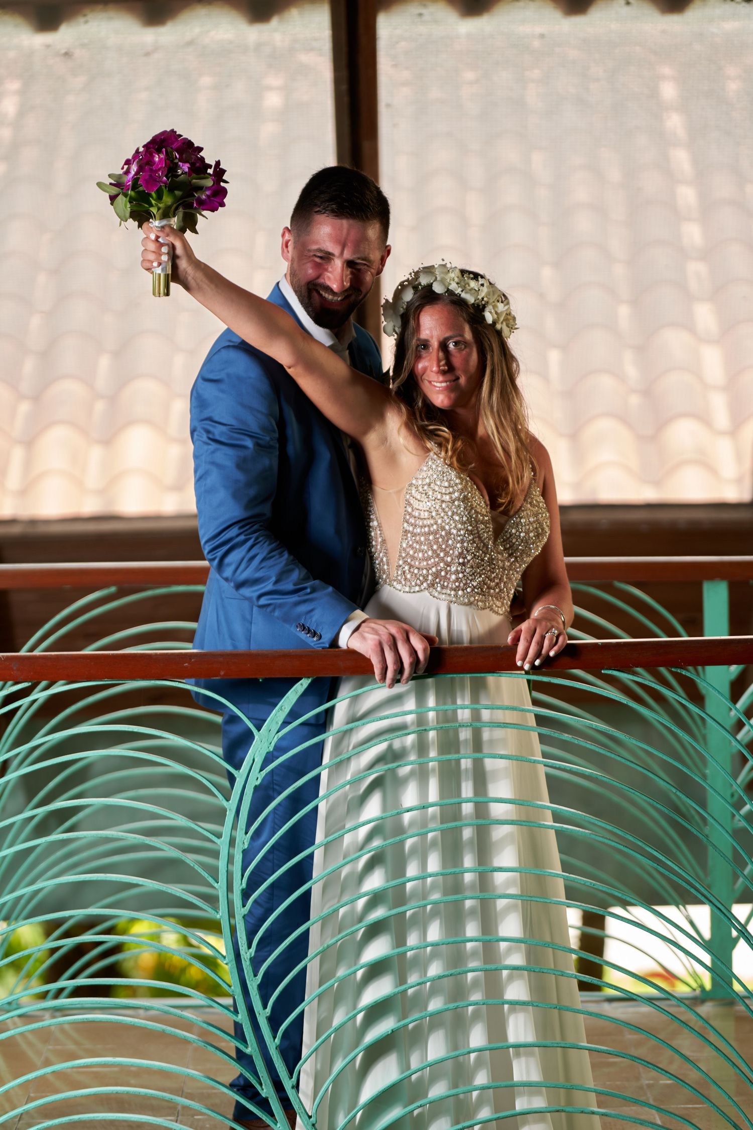 A couple in wedding attire share intimate moments near tropical palm fronds at an outdoor venue.