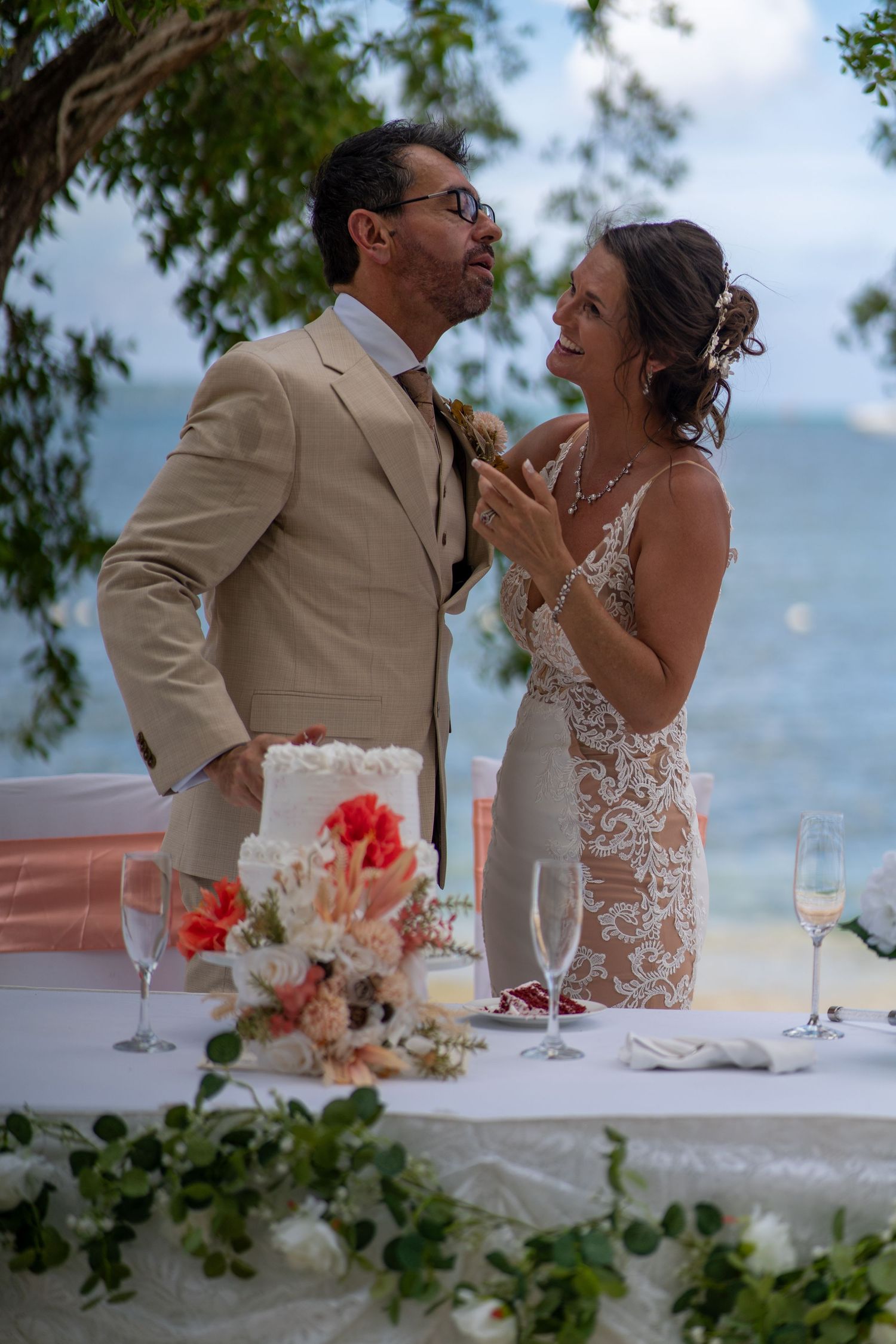 A romantic moment captured between newlyweds at an outdoor beach wedding reception with table settings and floral decor.
