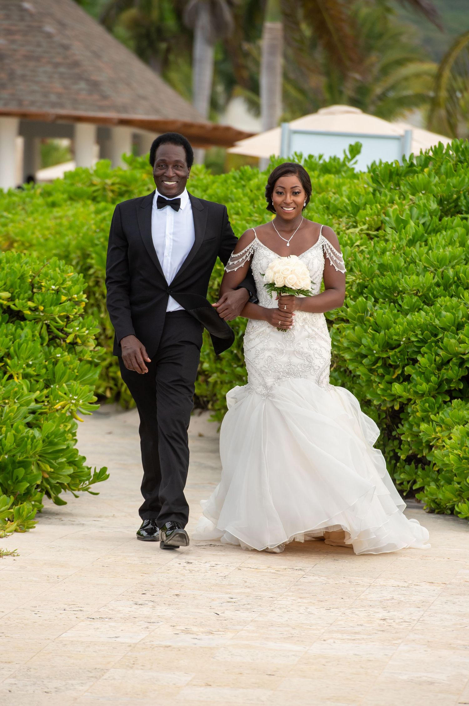 Wedding couple playfully runs together on a tropical beach path lined with lush greenery.