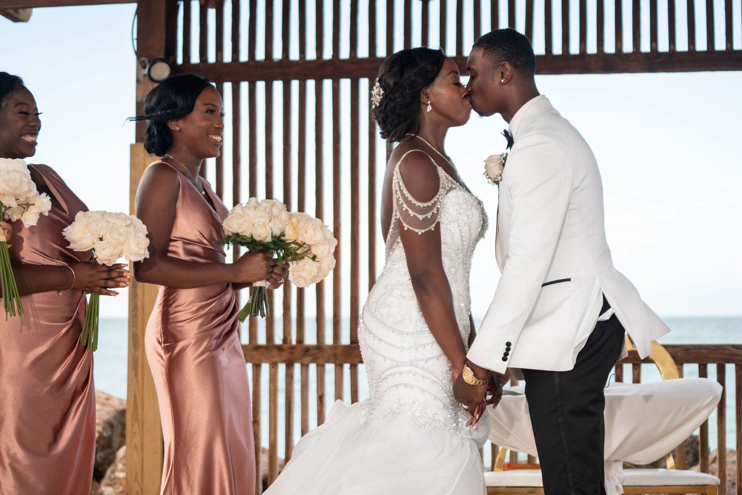 Elegant wedding party in rose gold bridesmaid dresses posing together at a beach ceremony with natural decor.