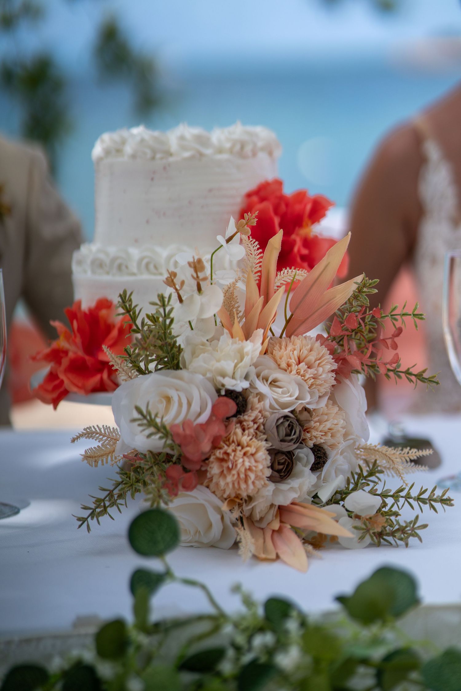 Close-up of delicate floral table decorations featuring pink and red carnations with greenery against a blurry background.