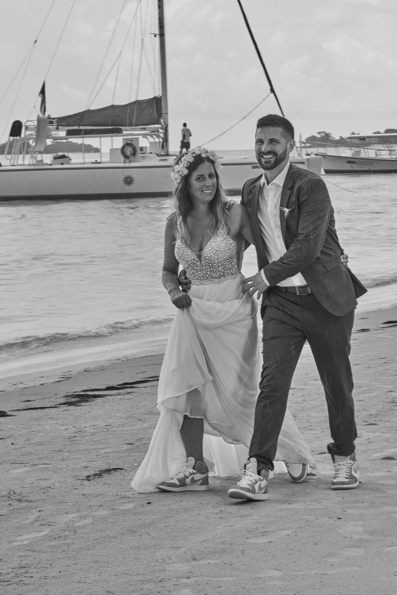 Black and white images of a couple in wedding attire and sneakers posing together on Negril beach near boats and water.