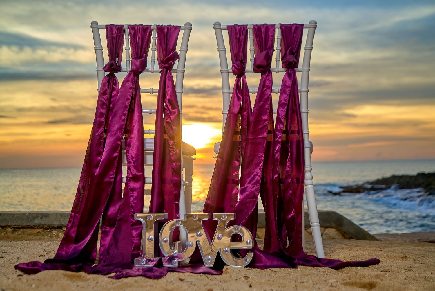 Bridesmaids in purple dresses silhouetted against a golden sunset on the beach.