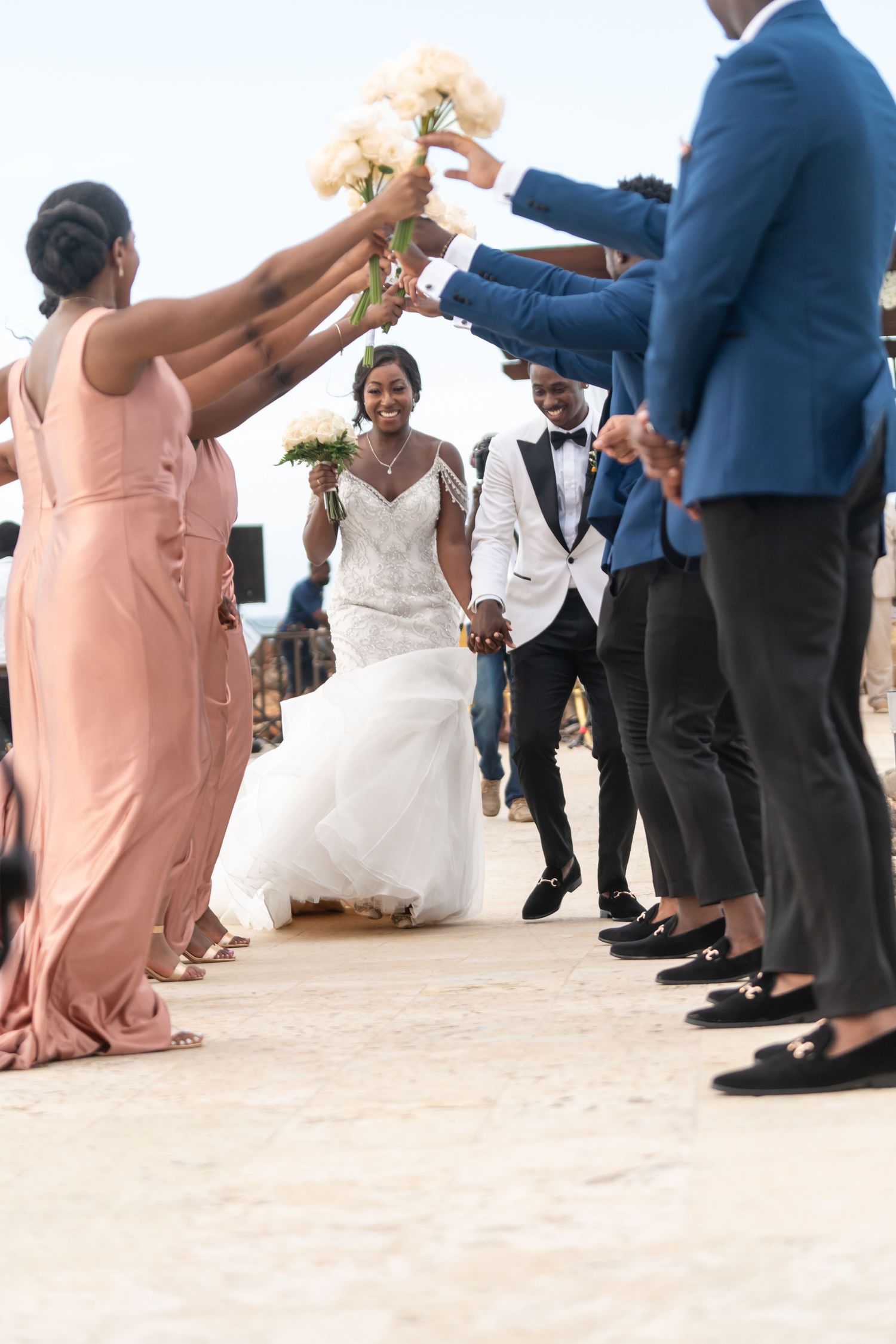 Wedding party guests dance together on a beach in formal attire including navy suits and peach dresses.