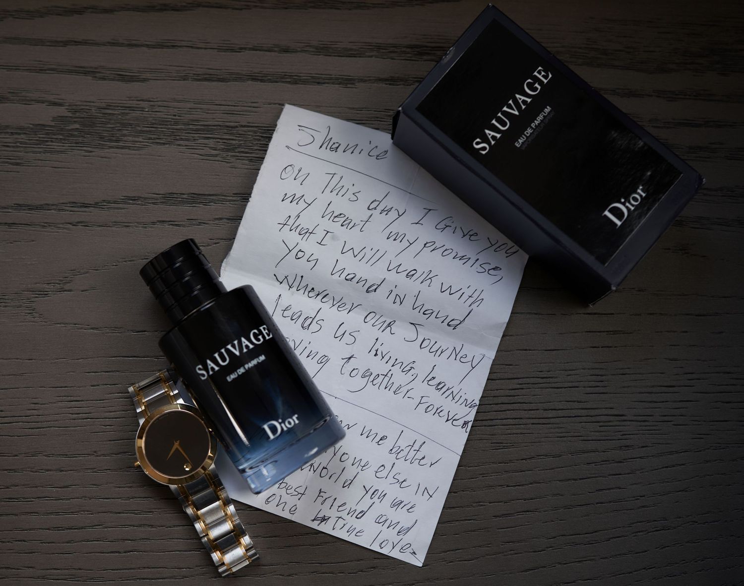 Luxury fragrance bottles from Dior arranged with handwritten notes and a gold watch on dark wooden surface.