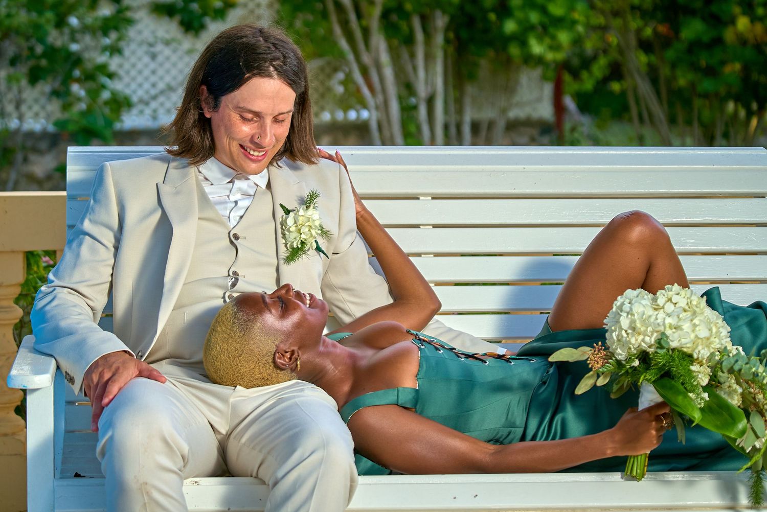 Person wearing tan suit sits on white bench with flowers and decor elements at outdoor event setting.