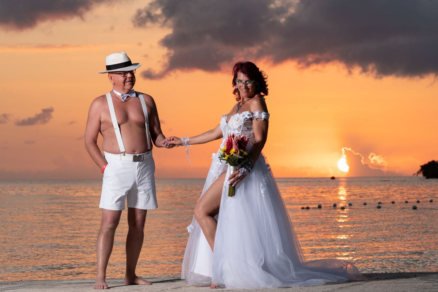 Newlywed couple shares romantic moments on a tropical beach at sunset with ocean waves in the background.