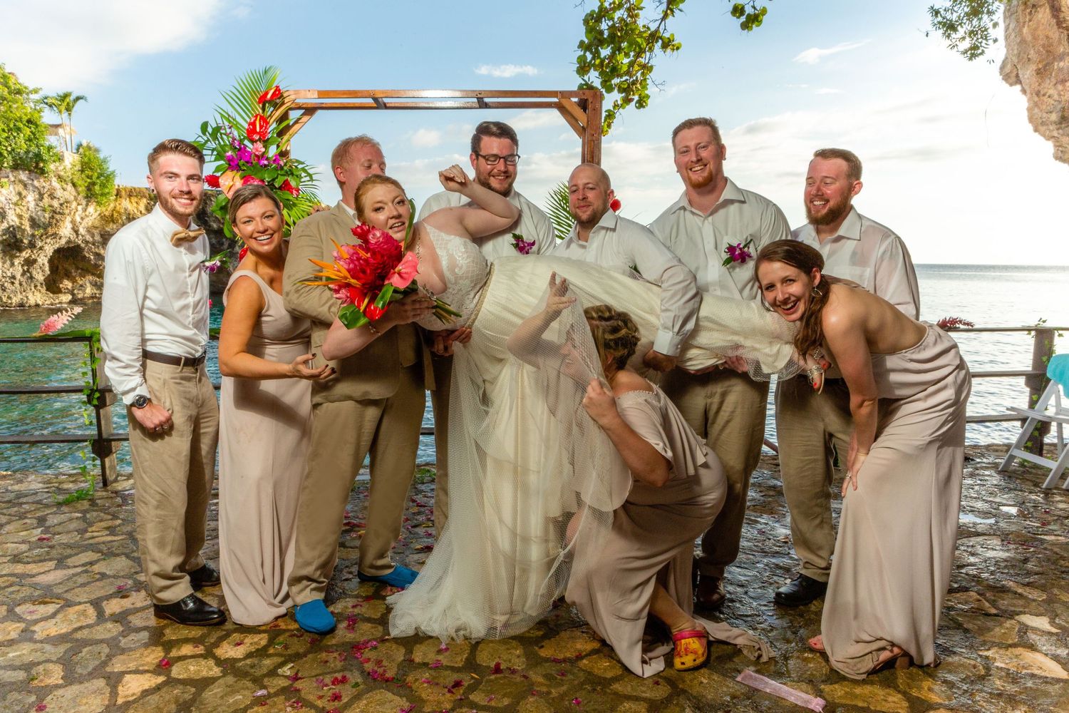 Wedding party in beige attire poses playfully on a rocky beach in Negril for a fun outdoor photo session.