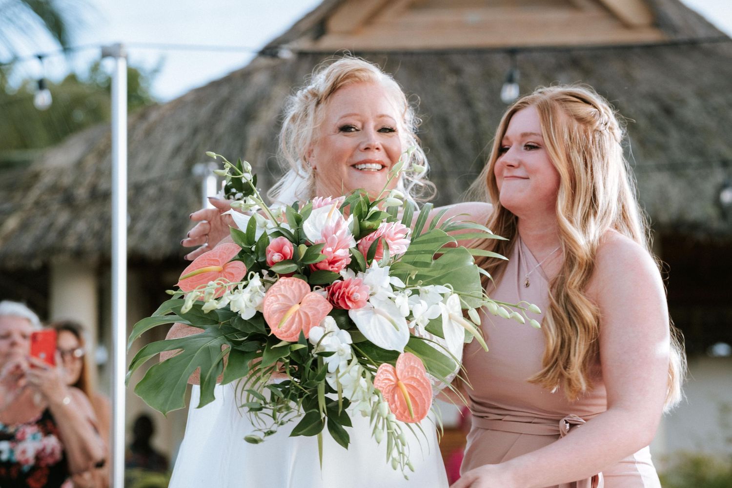 A celebratory wedding moment outdoors with flowers and expressions of joy on the bride's face during the ceremony.
