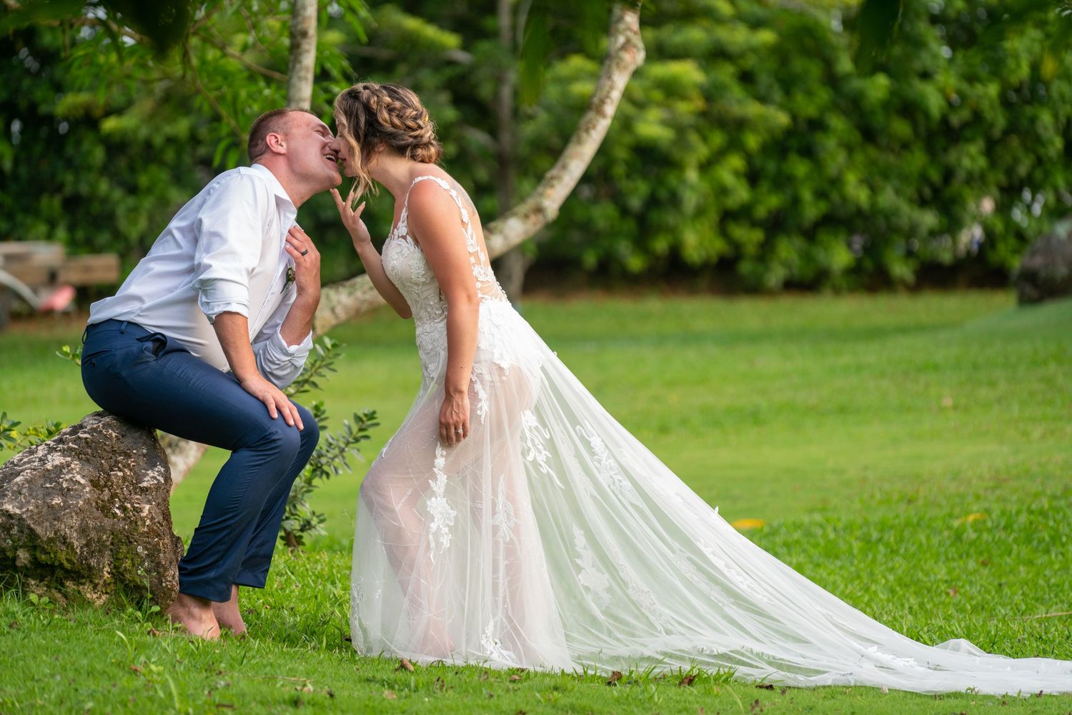 A couple shares an intimate moment in the grass on a sunny day at a wedding venue outdoors.