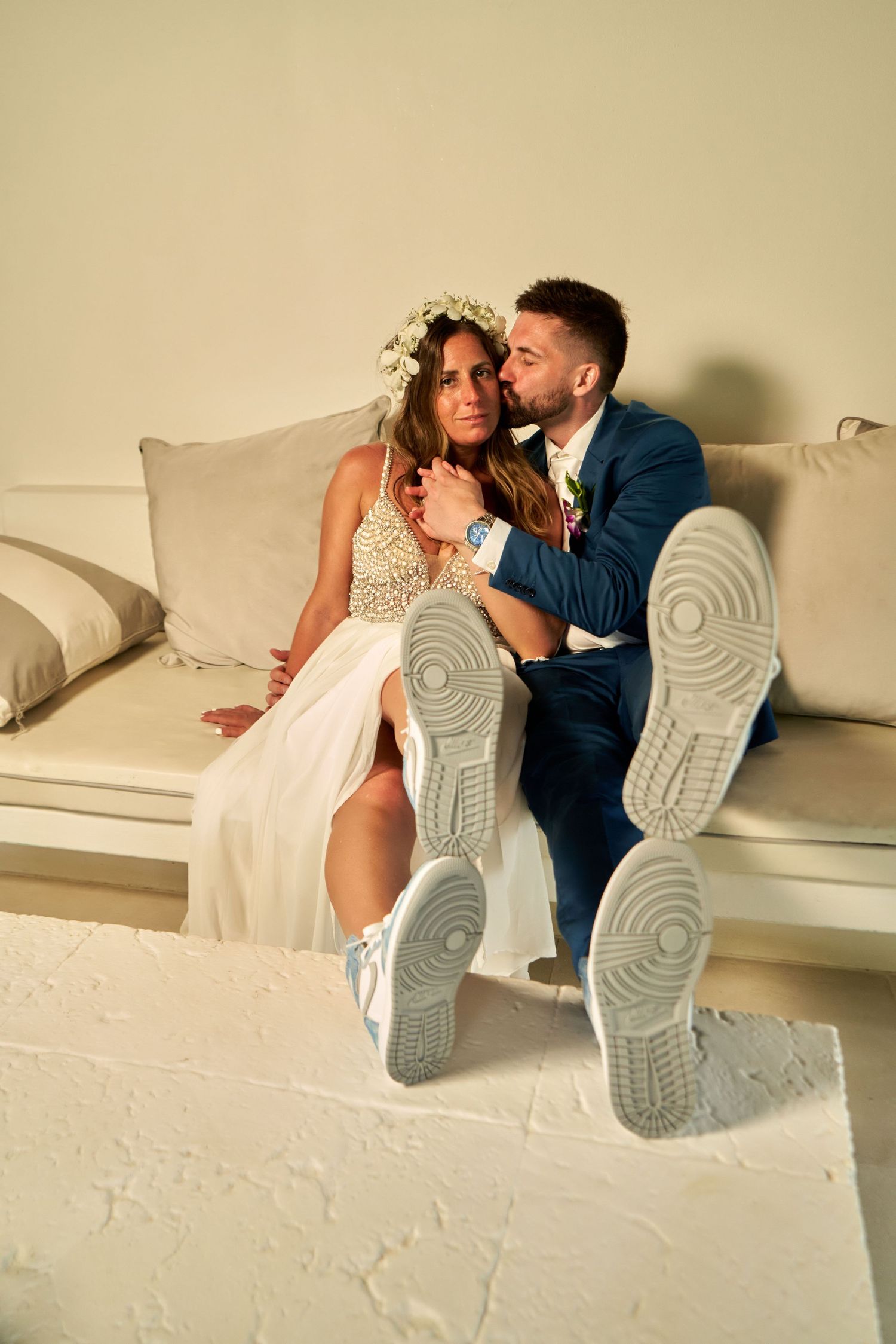 A couple in wedding attire lies playfully on a white couch showing off their sneakers in a series of candid shots.