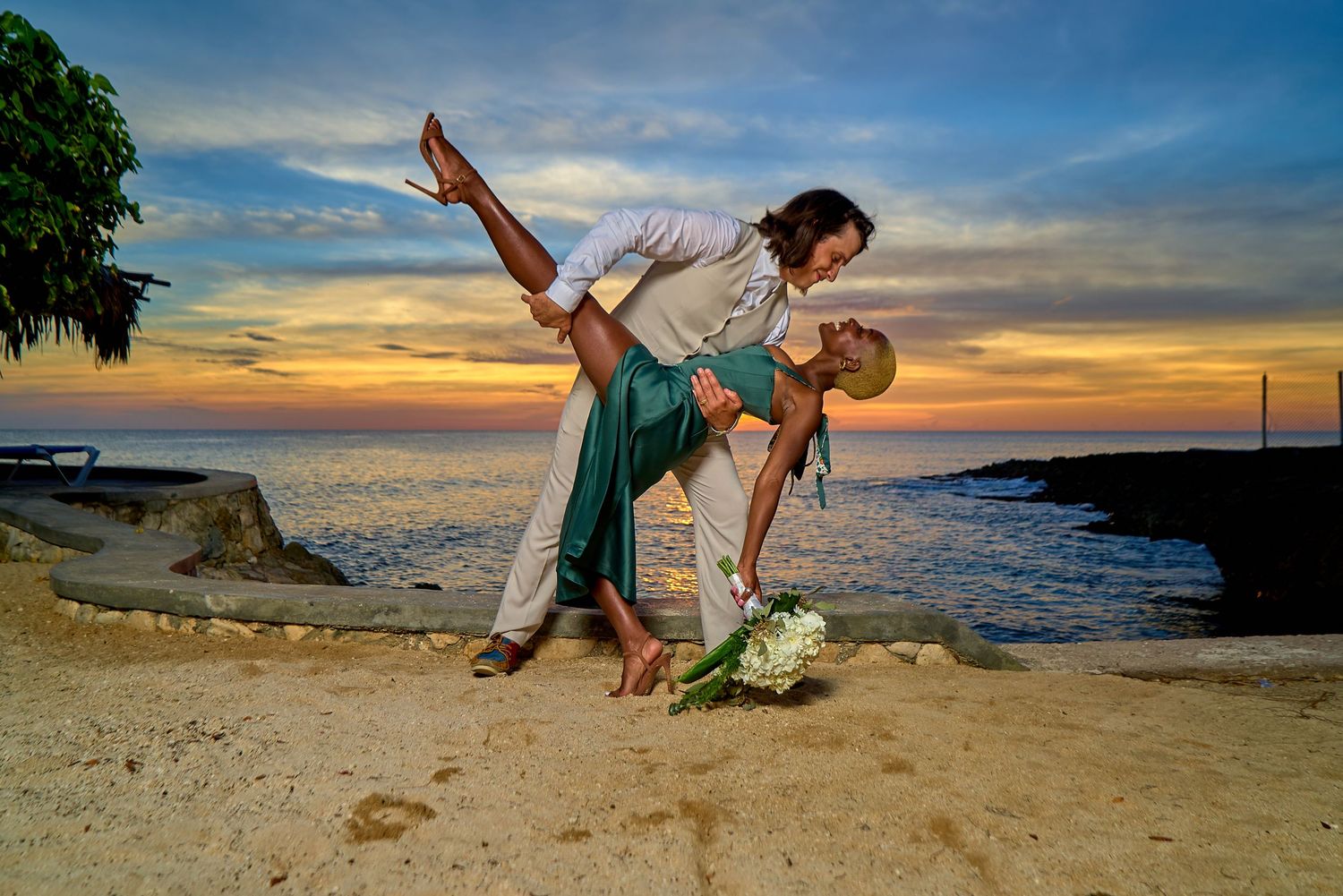 Playful beach wedding photo session during sunset with silhouettes against orange sky.