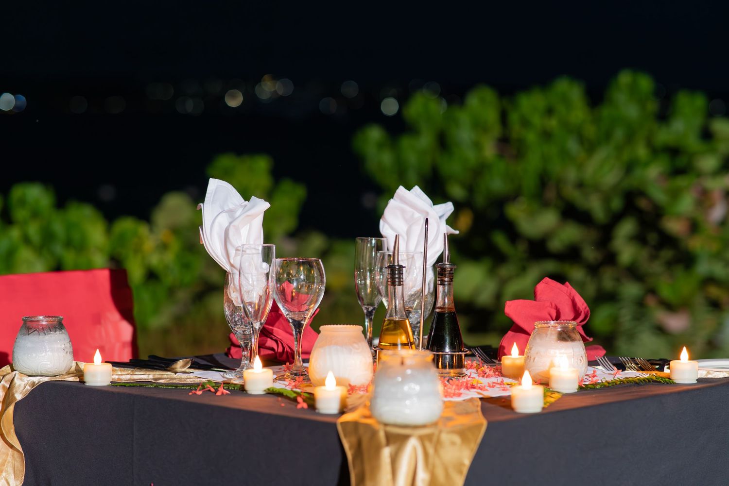 Flickering candlelight illuminates a romantic outdoor dining table with wine glasses and elegant settings at dusk.