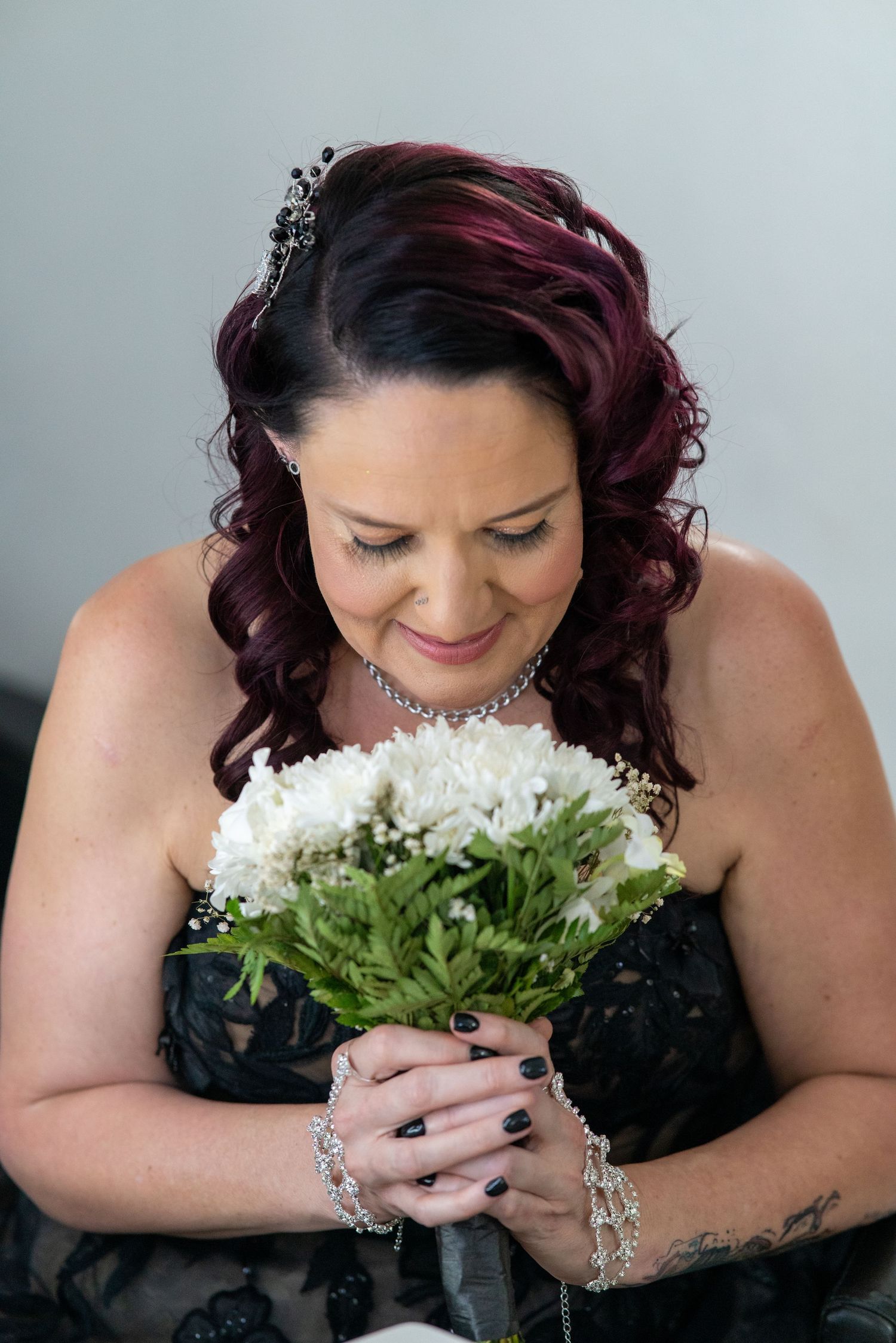 Artistic wedding portrait showing bride with burgundy hair holding white flowers while wearing black wedding dress.