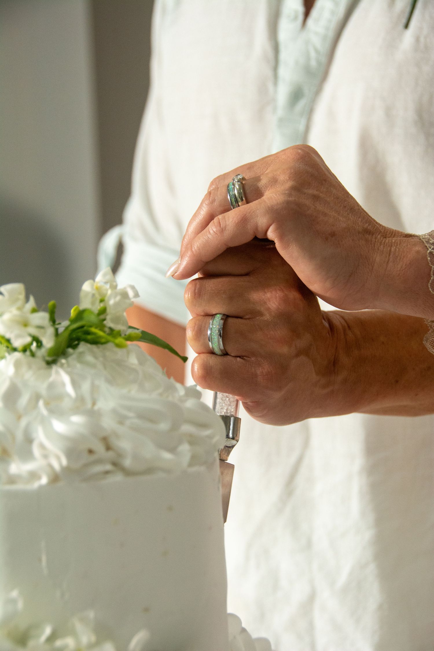 Close up of hands with rings hold knife to cut wedding cake